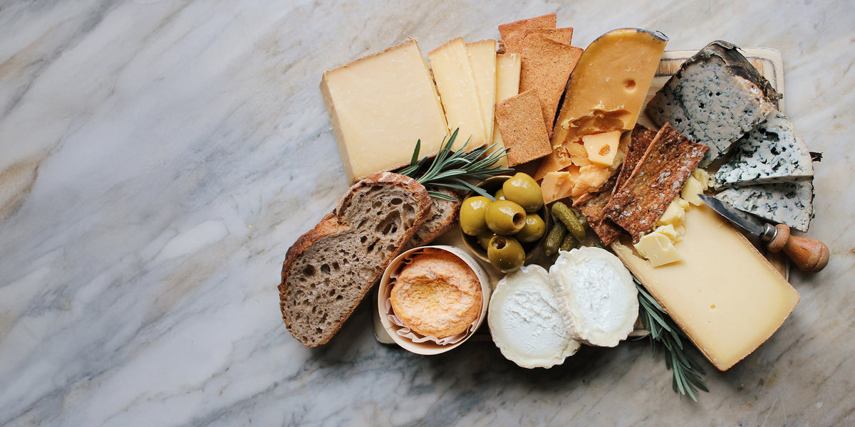 A Cheese Society cardboard delivery box with the circular logo, seen from above on a pale wooden table