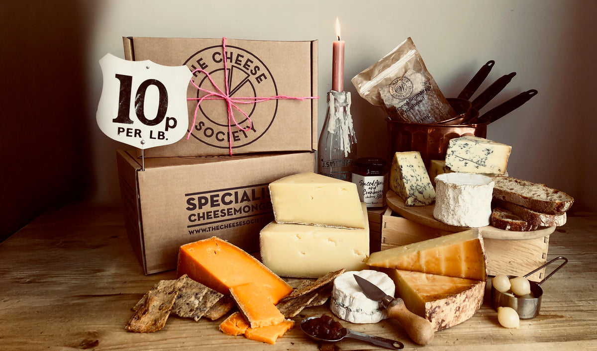 A Cheese Society cardboard delivery box with the circular logo, seen from above on a pale wooden table